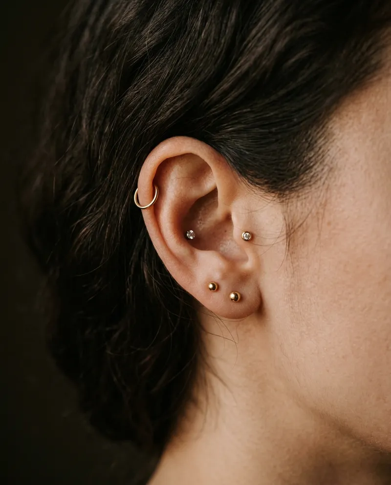 Orelha com vários piercings pequenos em ouro e titânio